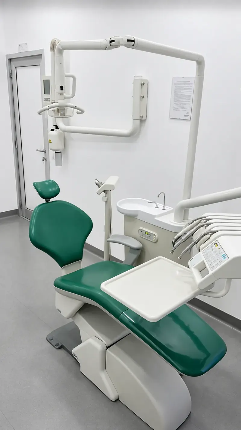 Sala operativa dello studio con il riunito verde, la lampada e il braccio radiografico, in un ambiente bianco e luminoso