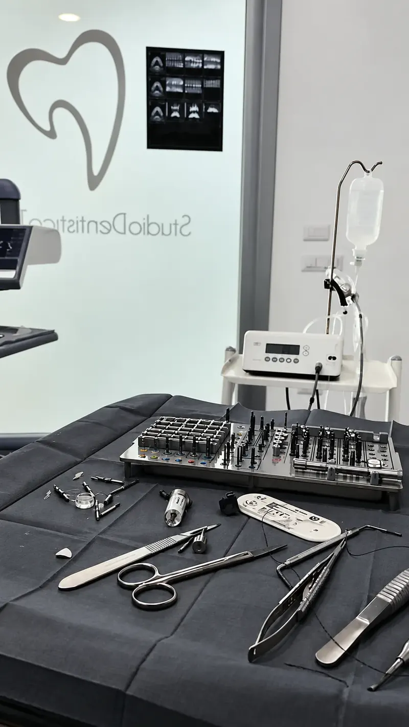 Strumentario chirurgico disposto sul telo sterile, con il kit per implantologia; sul vetro, il logo dello studio visto dal retro